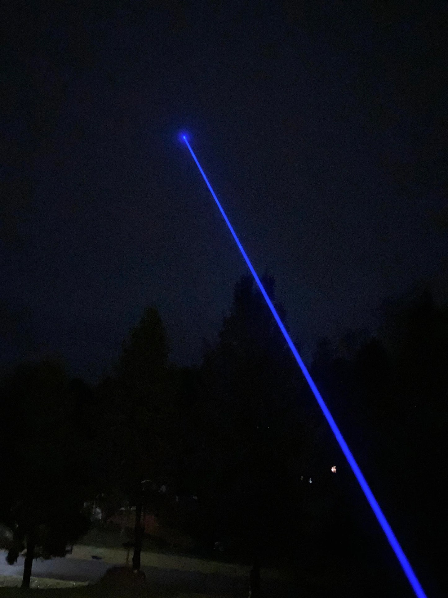 Blue laser pointer pointing upwards against a dark night sky with trees below.